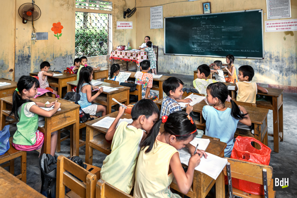 Enfants d'une école primaire travaillant sur pupitres dans leur classe avec l'institutrice vers Hué, Annam, Vietnam